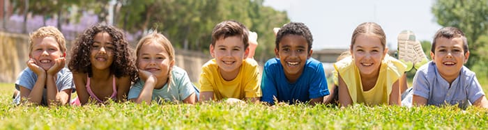 Group of children laying shoulder to shoulder in the grass.