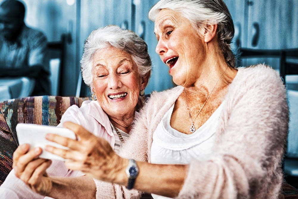 Photo of two seniors smiling at a phone.