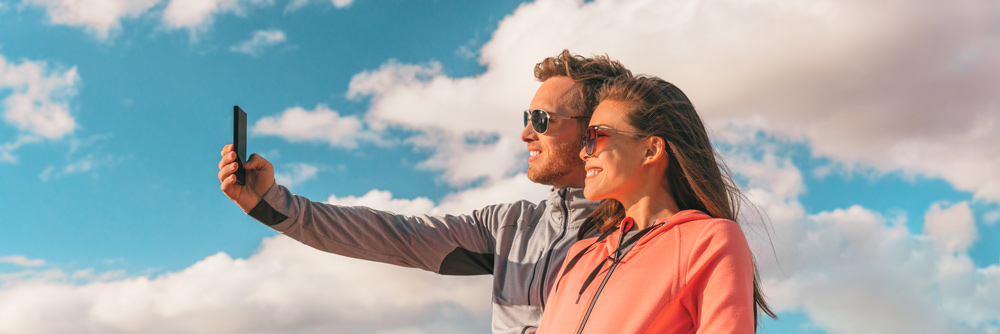 Man and woman wearing sunglasses while holding phone.