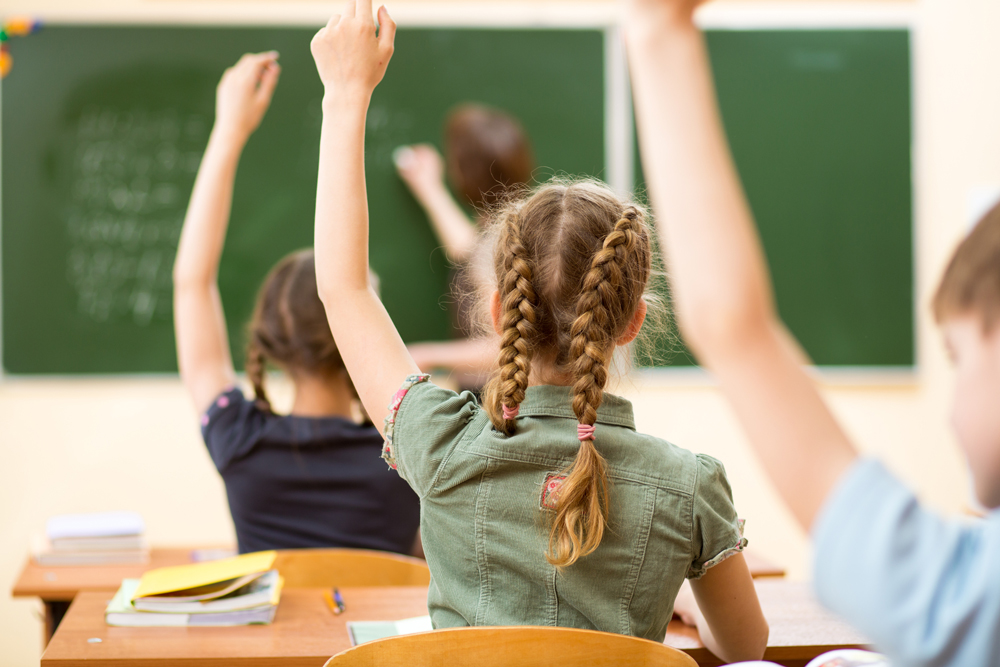 Kids in a classroom raising their hands